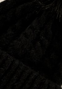 Gorro negro de punto hecho de lana suave y texturada, con una banda acanalada en la parte inferior y un pompón de piel en la parte superior.
