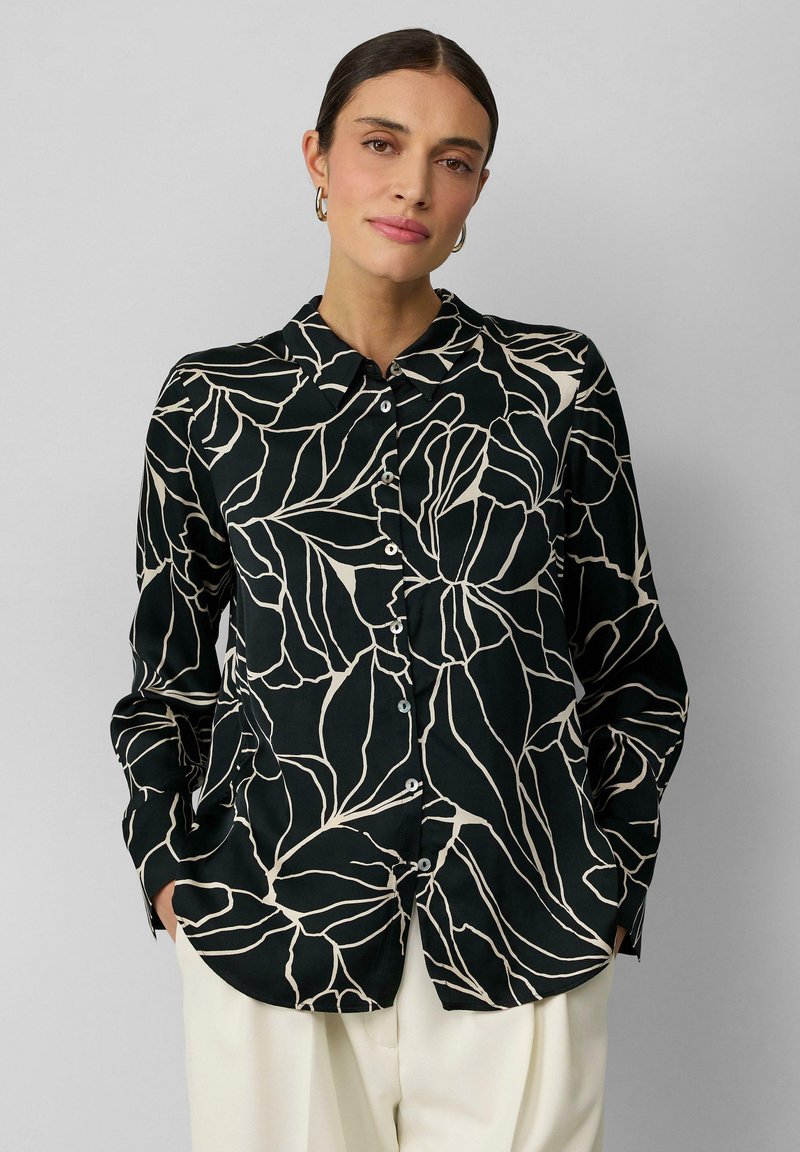 Zwarte overhem shirt met wit bladdessin, featuring een kraag en lange mouwen, gemaakt van een gladde stof. Gdragen met crèmekleurige broek.