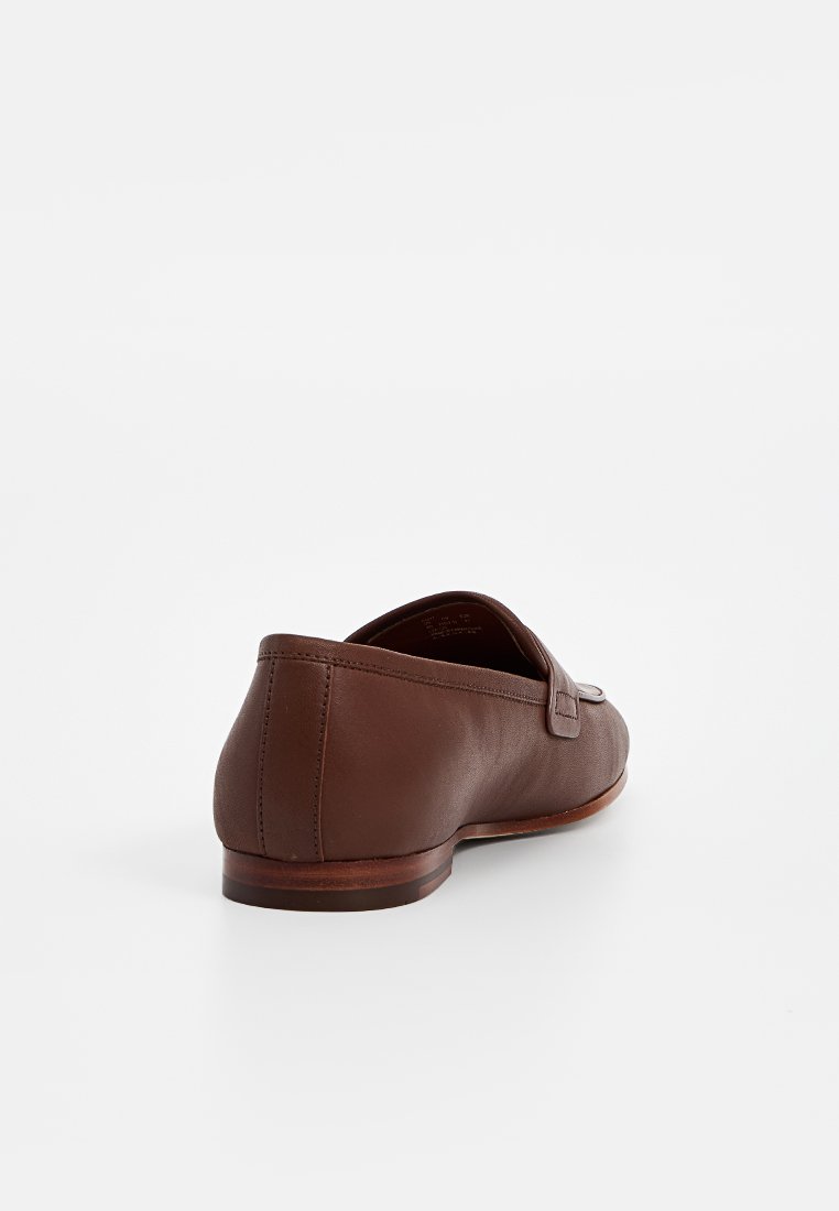 Mocassins en cuir marron avec une texture lisse, talon plat et une boucle décorative. Design simple et forme épurée.