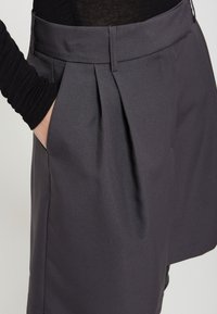 Grijze geplooide shorts met een gladde stofstructuur, met een hoge tailleband en zijzakken, gezien vanuit een lichte hoek.