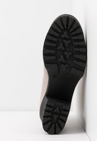 Semskade ankelskor med en beige ovandel och svart gummisula, som har ett texturerat mönster för grepp och förbättrad hållbarhet.