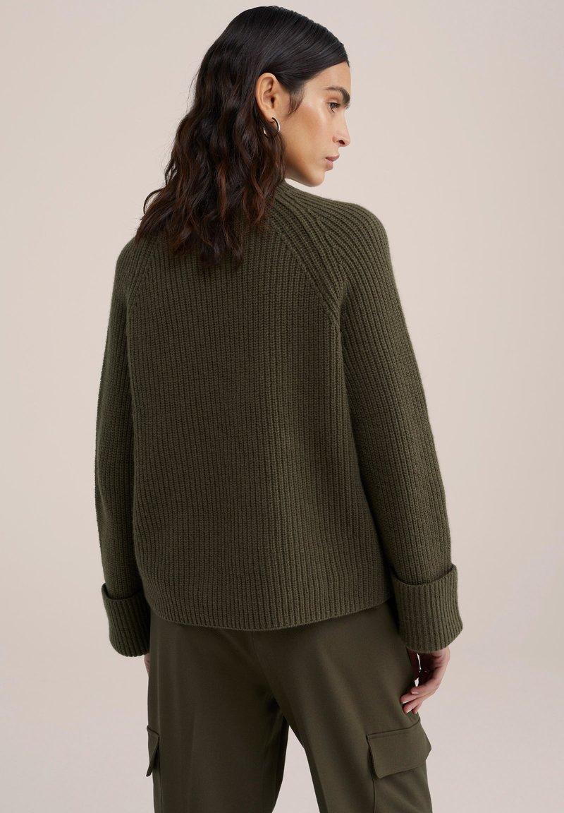 Oliwkowy, prążkowany sweter o luźnym kroju, z opadniętymi ramionami i szerokimi mankietami, zestawiony z pasującymi oliwkowymi spodniami.