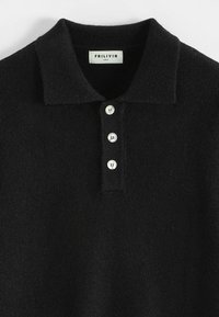 Polo shirt noir en tissu texturé avec col, comportant quatre boutons en argent le long de la patte de boutonnage et une étiquette à l'intérieur.