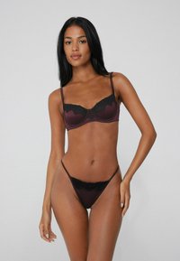 Burgundy bra and thong set featuring lace accents, adjustable straps, and a smooth texture, designed with a delicate scalloped edge.