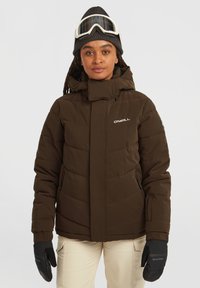Bruine pufferjack met een hoge kraag, voorzien van een ritssluiting, zijzakken en een gewatteerde textuur. Gekleed met zwarte handschoenen en een grijze beanie.