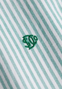 Tissu à fines rayures verticales vertes et blanches avec des initiales de monogramme vertes brodées au centre.