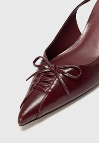 Burgundy nahka slingback -kengät, joissa on terävä kärki, korostettuina nauha ja kerrostettu pinta varpaissa. Sileä, kiiltävä pinta.