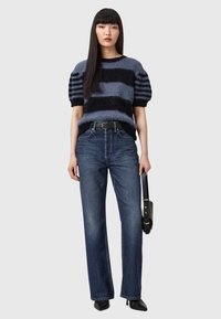 Gestreifter Strickpullover in Blau und Schwarz mit Puffärmeln, kombiniert mit hoch taillierten dunklen Jeans und schwarzen spitzen Schuhen.