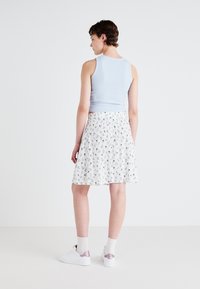 Lys blå ribbet tank topp kombinert med en hvit blomstrete A-linje skjørt, med blå og grønne mønstre, fullført med hvite joggesko og sokker.