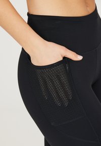 Leggings de sport noirs avec poche latérale en maille, texture lisse, taille haute et coutures plates pour le confort et le style.