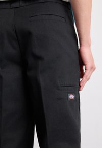 Black cargo pants made of thick fabric, featuring side pockets and a visible logo patch on the thigh, with a smooth texture and fitted design.