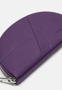 Lila Lederbörse mit abgerundetem Design, sichtbaren Nähten und Reißverschluss. Hat eine glatte Textur und ein geprägtes Markenlogo.