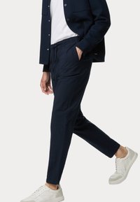 Pantaloni blu navy a trama con elastico in vita e tasche laterali, abbinati a una giacca coordinata e scarpe da ginnastica bianche.