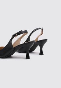 Zapatos de tacón negro tipo slingback con punta redondeada, acabado de cuero brillante, tira ajustable en el tobillo y tacón acampanado de 6 cm para mayor estabilidad.