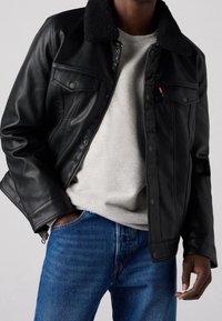 Black leather jacket with a fur collar, two front pockets, and a zip closure, worn over a light gray sweatshirt and blue denim jeans.