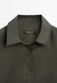 Chemise vert foncé en tissu texturé. Dotée d'un col classique, d'une fermeture à boutons et d'une poche poitrine. L'étiquette indique "Massimo Dutti."