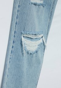 Ljusblå denimjeans med slitna områden och fransade kanter, som visar en avslappnad design och en subtil textur.