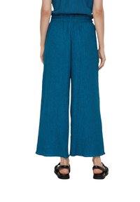 Teal wijd-uitlopende broek van gestructureerde stof met een hoge taille en een biesdetail, gecombineerd met zwarte bandjessandalen.