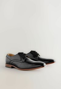 Zwarte leren dresschoenen met een spitse neus, gedetailleerde stiksels en een bruine houten zool. Ze hebben een vetersluiting en geperforeerde accenten.