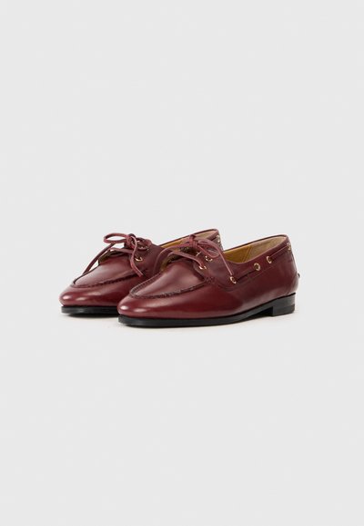 Burgundy leather loafers with rounded toe, decorative stitching, and lace-up design. Features gold eyelets and minimal heel height.