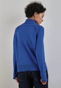 Königsblauer Pullover mit hohem Kragen, gerippten Bündchen und Saum, der über texturierte Muster an den Schultern und am Rücken verfügt.