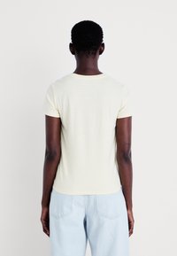 T-shirt z krótkim rękawem w jasnożółtym kolorze z poziomymi paskami, o miękkiej fakturze, z okrągłym dekoltem i dopasowanym krojem, zestawiony z jasnoniebieskimi dżinsami.