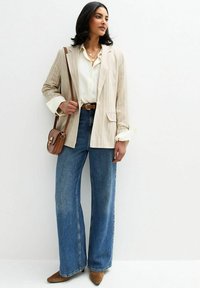 Beige randig kavaj, vit skjorta, brun bälte, vida blå jeans och bruna klackboots. Axelremsväska med detaljer i guldspänne.