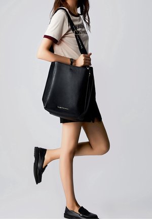 Sort læder tote taske med pebret tekstur, udstyret med lynlås lukning og justerbar rem. Simpelt design med et minimalistisk logo.