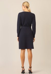 Abito lavorato a maglia blu navy con maniche lunghe, vita aderente e gonna svasata, caratterizzato da una trama liscia e un design minimalista.