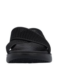 Black sandals with a textured sole and cross-over mesh straps. Lightweight design features a cushioned footbed for comfort.