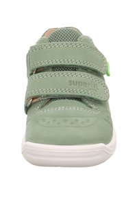 Grüner Lederschuh mit Netzakzenten, zwei Klettverschlüssen und einer weißen Gummisohle. Verfügt über Nähte und kleine Perforationen an der Zehenpartie.