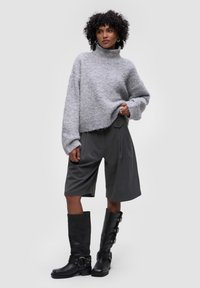 Šedý, huňatý svetr s rolákem a volným střihem, spárovaný s tmavě šedými skládacími šortkami. Černé vysoké boty ke kolenům s přezkami a pásky.