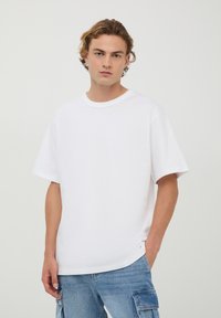 T-shirt bianco a maniche corte realizzato in morbido cotone, caratterizzato da una vestibilità rilassata e scollatura a girocollo, abbinato a pantaloni cargo blu.