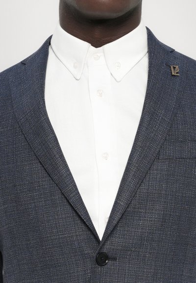 Marineblaues Blazer aus strukturiertem Stoff, mit einem einreihigen Knopfverschluss und einem Reverskragen, kombiniert mit einem weißen Hemd mit Knöpfen darunter.
