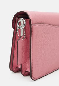 Sac à main en cuir rose avec une finition texturée, équipé d'un fermoir en métal argenté et d'une étiquette. Le design comprend des accents marron foncé et des coutures.