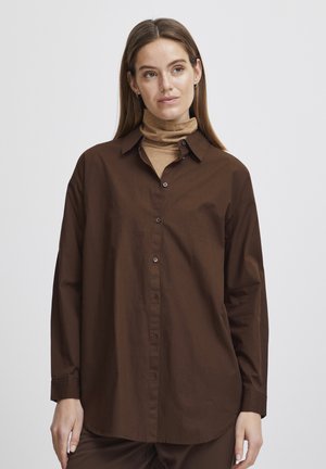 Brown button-up shirt with a relaxed fit, long sleeves, and a classic collar. Worn over a tan high-neck top, featuring a smooth texture.
