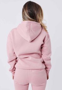 Sudadera con capucha rosa polvoriento de textura suave y capucha. Tiene puños y dobladillo acanalados, combinada con pantalones ajustados a juego.