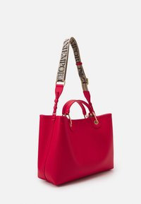 Czerwona torba tote z ekoskóry o konstrukcyjnym designie, złotym metalowym wykończeniem, podwójnymi górnymi uchwytami i ozdobnym regulowanym paskiem na ramię.
