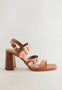 Sandale à talon haut en cuir marron avec trois sangles réglables, accents en métal doré et un bout carré. Talon en bois sculpté.