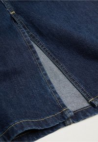 Tumma farkkuhousut, joissa on sivupistoissa yksityiskohtia, vaaleansininen sisus, ja keltaista tikkausta saumoissa lisäyksinä.