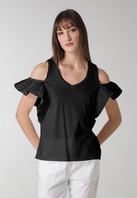 Sort kortærmet top med cold-shoulder design, prydet med volanger og en V-udskæring. Fremstillet af letvægtsstof.
