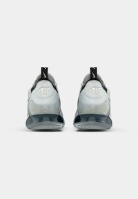 Pár bílých a šedých tenisek Nike Air zobrazených zezadu, s černými poutky s bílými logy Swoosh a viditelnými podrážkami s vzduchovou vložkou.