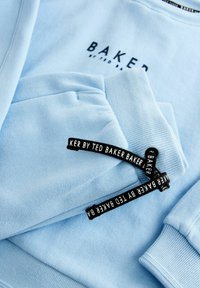 Svetlomodrý mikina vyrobená z mäkkého materiálu. Má rebrované manžety a lem. Obsahuje čierne štítky s nápisom "BAKER by TED BAKER" v bielej farbe.
