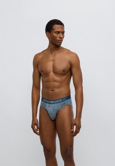 Pánské slipy s modrým páskem s nápisem „Emporio Armani“, vzorovaná látka v různých odstínech modré a šedé, těsný střih.