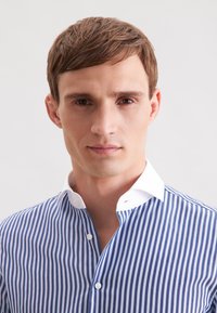 Camicia button-up con righe verticali blu e bianche, colletto bianco a contrasto. Tessuto leggero, design aderente e bottoni semplici.