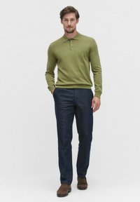 vihreä pitkähihaisen polo-paita, jossa on kolme nappia, yhdistettynä tummansinisiin siistihin housuihin ja ruskeisiin kenkiin. Asusteessa on istuva muotoilu.