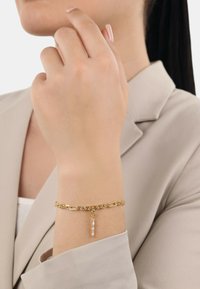 Pulsera de cadena de oro con eslabones alargados y un colgante en forma de barra. Los eslabones tienen un acabado brillante y el charm añade un detalle delicado.