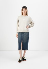 Sudadera beige con el logo "GAP", falda midi de mezclilla con abertura frontal y zapatillas negras con diseño de cordones y suela marrón.