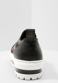 Czarne skórzane sneakersy z kontrastowym brązowym wzorem w kamuflaż, biała gumowa podeszwa i teksturowana wszywka na pięcie. Widok z tyłu, gładkie wykończenie.