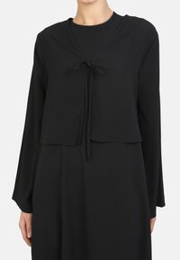 Schwarzes, kurzes Oberteil mit langen Ärmeln und einer Frontbindedetail. Hergestellt aus leichtem, strukturiertem Stoff, bietet es eine lockere Passform und ein minimalistisches Design.